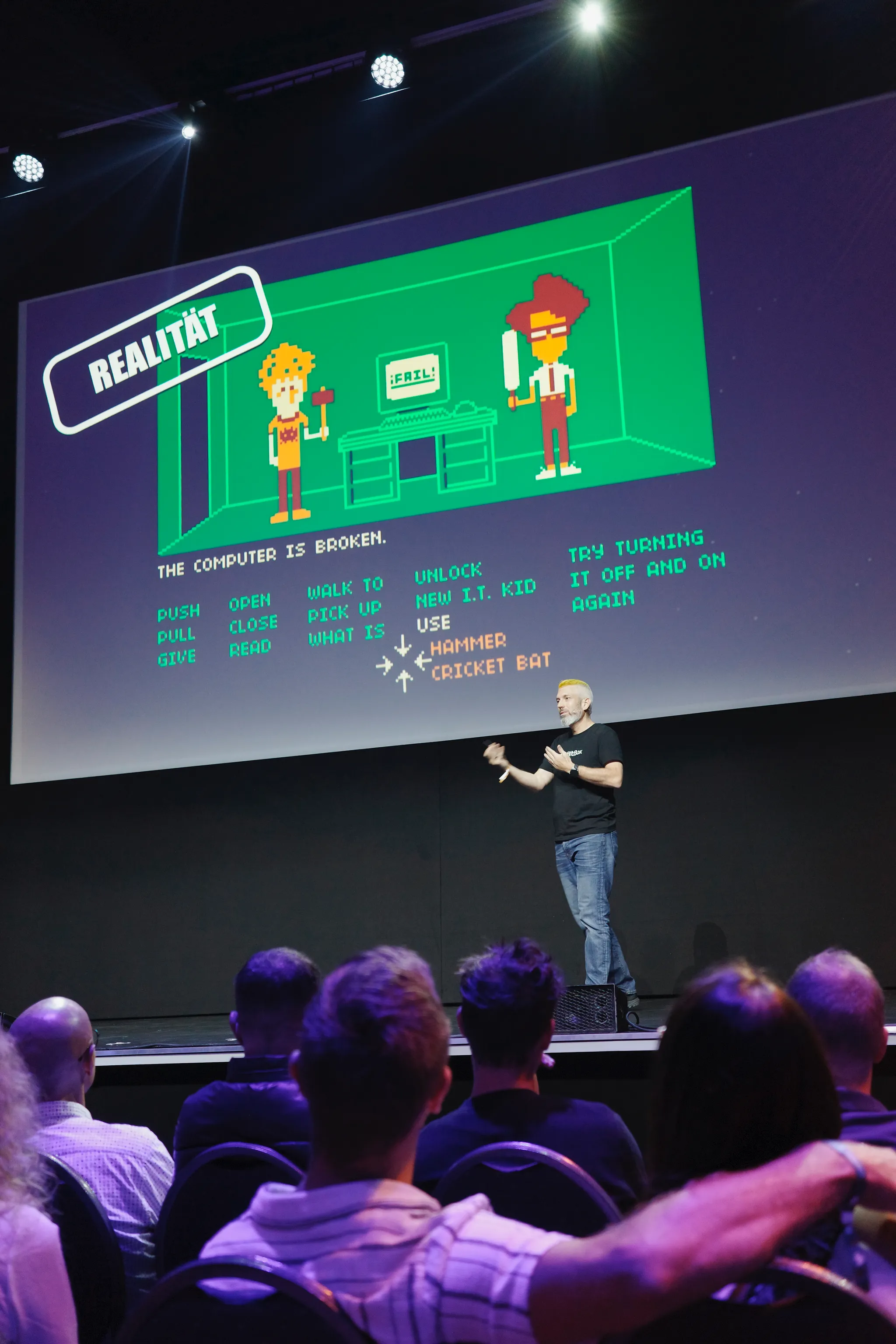 Stadicus on stage in front of a pixel-art slide titled 'Realität'